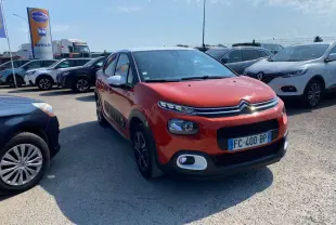 Citroën C3 orange vue 3/4 avant droit avec protections latérales noires et toit noir dans un parking.