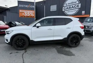 Profil côté gauche d'un Volvo XC40 blanc avec jantes alliage noires, garé devant un garage commercial.