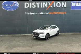 DS7 Crossback blanc en 3/4 avant droit, avec calandre noire et jantes noires, devant un mur gris marqué Distinxion