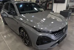 Peugeot 308 gris Sélénium vue 3/4 avant droit en showroom, avec calandre noire distinctive et jantes bicolores.