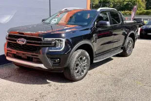Ford Ranger 3.0 V6 Wildtrak Plus noir agate, vue 3/4 avant droit avec jantes alu et barres de toit visibles.