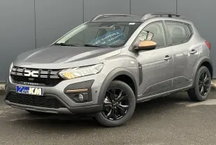 Dacia Sandero Stepway TCE 110 gris schiste en 3/4 avant droit avec jantes noires et barres de toit grises.