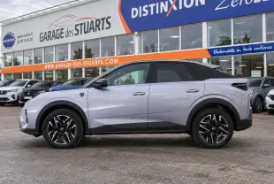Vue de profil côté gauche du Peugeot 3008 gris Artense avec jantes alliage noires et toit noir, devant un garage.