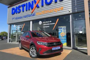 Volkswagen Taigo rouge roi en 3/4 avant droit devant un showroom Distinxion, avec jantes alliage et calandre noire.