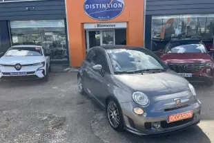 Vue 3/4 avant droite d'une ABARTH 500 gris foncé métallisé avec jantes alu et plaque "OCCASION" devant un garage.