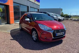 DS3 rouge avec toit blanc, vue 3/4 avant droit, garée devant un bâtiment commercial sous un ciel bleu.