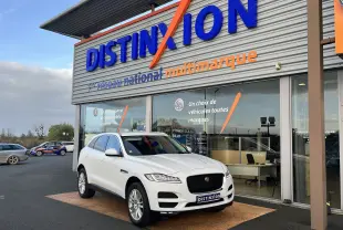 Jaguar F-PACE blanc en 3/4 avant droit, stationné devant un showroom Distinxion avec une calandre noire distinctive.
