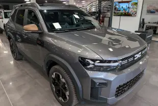 Vue 3/4 avant droite du Dacia Bigster Hybrid-G 150 4x4 Extrême gris schiste avec rétroviseurs bronze en showroom.