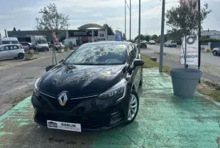 Renault Clio 1.0 TCE Evolution noir vue 3/4 avant droit, stationnée en extérieur sur sol vert avec reflet du ciel sur la carrosserie.