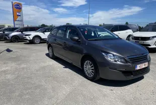 Peugeot 308 SW gris clair vue 3/4 avant droit sur parking ensoleillé avec attelage visible à l'arrière.