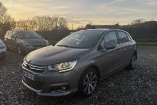 Citroën C4 II gris métallisé vue 3/4 avant droit au coucher du soleil sur un parking gravillonné.