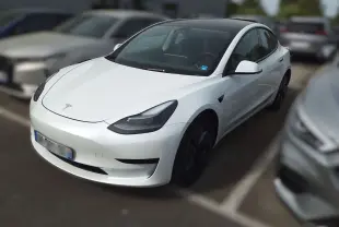 Tesla Model 3 blanc en 3/4 avant droit dans un showroom avec jantes noires et éclairage intérieur.