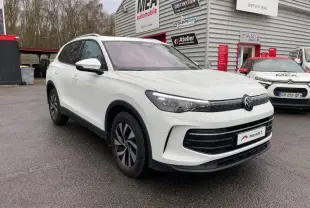Vue 3/4 avant d'un Volkswagen Tiguan blanc pur 2025 avec jantes alu et toit ouvrant panoramique, stationné devant un garage.