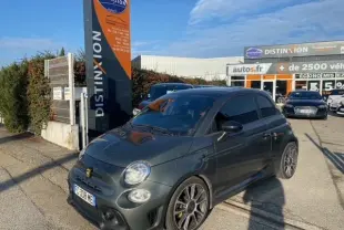 ABARTH 595 gris foncé en 3/4 avant droit, avec jantes sport et vitres teintées, stationné devant un concessionnaire.