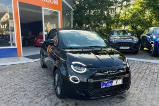 Vue 3/4 avant d'une FIAT 500 électrique noire stationnée devant un showroom avec phares LED ronds allumés.
