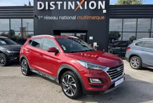 Hyundai Tucson rouge métallisé en 3/4 avant droit, avec jantes alliage et calandre chromée visible devant un bâtiment noir Distinxion.
