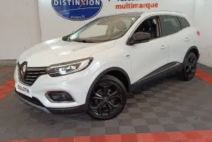 Renault Kadjar blanc vue 3/4 avant droit, jantes noires brillantes et phares LED allumés en intérieur showroom.