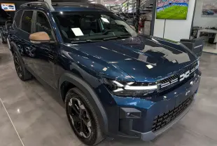 Vue 3/4 avant gauche du Dacia Bigster bleu indigo avec rétroviseurs couleur bronze en showroom.