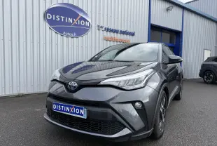Toyota C-HR 1.8 hybrid gris atlas vu en 3/4 avant droit devant un bâtiment commercial.