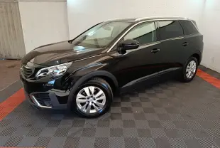 Peugeot 5008 noir vue 3/4 avant droit, avec jantes alliage et toit équipé de rails chromés dans un garage.