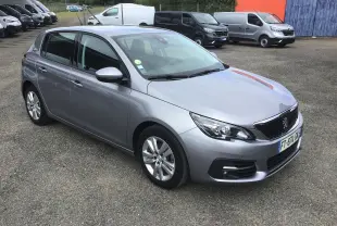 Peugeot 308 gris Artense vue en 3/4 avant droit, avec jantes alliage et calandre noire distinctive.