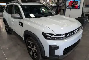 Vue 3/4 avant gauche d'un Dacia Bigster blanc glacier avec calandre noire et jantes bi-ton en showroom.