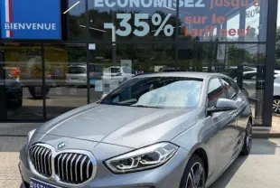 BMW Série 1 118d Edition Sport gris foncé vue 3/4 avant, avec calandre et phares LED distinctifs, devant un showroom multimarque.