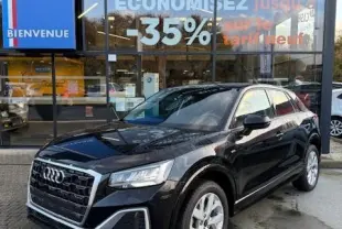 Audi Q2 noir vue 3/4 avant droit, garée devant une concession Distinxion avec reflets sur la carrosserie.