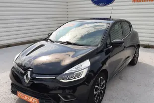 Renault Clio IV noire vue 3/4 avant droit, avec phares LED et jantes alliage bicolores, stationnée devant un mur blanc.