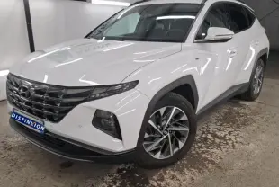 Hyundai Tucson blanc en 3/4 avant droit, avec jantes alliage et calandre chromée dans un showroom.