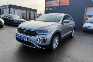 Volkswagen T-Roc gris pyrite vu en 3/4 avant droit sur parking devant un bâtiment commercial autos.fr