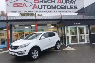 KIA Sportage blanc en 3/4 avant droit stationné devant un garage avec enseigne Brech Auray Automobiles.