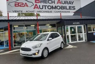 Ford KA+ blanc Gold vue 3/4 avant droit avec calandre chromée et feux allumés devant un garage Brech Auray Automobiles
