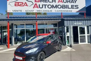 Ford Fiesta noire vue en 3/4 avant droit, avec rétroviseurs rouges et jantes noires, devant un garage Brech Auray Automobiles.