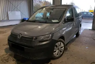 Vue 3/4 avant droit du Volkswagen Caddy Maxi gris Pure Grey, avec pare-chocs noir et jantes acier en intérieur d'atelier.
