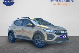 Vue 3/4 avant droit de la Dacia Sandero Stepway beige Safari avec barres de toit et jantes foncées.