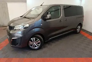Peugeot Traveller gris clair vu en 3/4 avant droit dans un garage avec jantes alliage et vitres teintées.