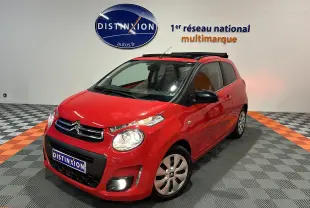 Citroën C1 rouge vue 3/4 avant droit, toit ouvrant Airscape ouvert, dans un showroom avec sol gris et orange.