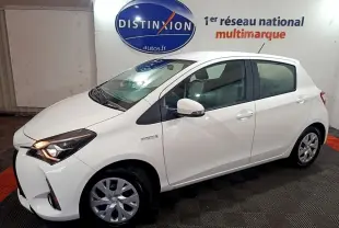 Toyota Yaris hybride blanche vue de profil côté gauche, avec phares allumés et logo Distinxion en arrière-plan.