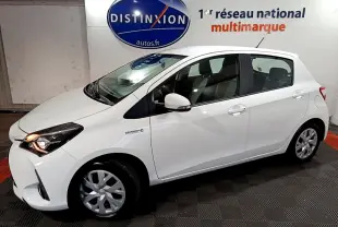 Vue de profil droit d'une Toyota Yaris 1.5 Hybride blanche avec feux avant allumés dans un showroom.