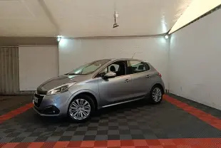 Peugeot 208 Puretech 82 Allure gris clair vue 3/4 avant droit dans un garage éclairé.
