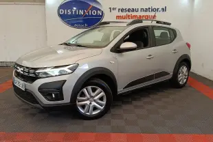 Vue 3/4 avant droit d'une Dacia Sandero Expression gris clair avec barres de toit et jantes alliage en showroom.