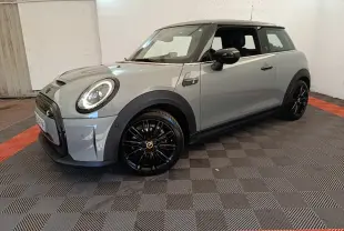 Vue 3/4 avant gauche d'une MINI Cooper SE gris clair avec jantes noires et toit noir dans un intérieur fermé.