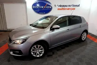 Peugeot 308 Puretech gris clair vue 3/4 avant droit, phares allumés, dans un showroom intérieur.