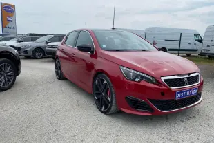 Peugeot 308 GTi rouge vue 3/4 avant avec jantes noires et calandre chromée sur parking extérieur.