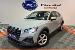 Audi Q2 gris en 3/4 avant droit, phares allumés, sur sol damier avec logo Distinxion en arrière-plan.