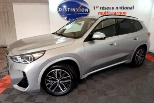 BMW X1 xDrive23i M Sport gris clair vue de profil droit en intérieur avec jantes noires et toit noir.