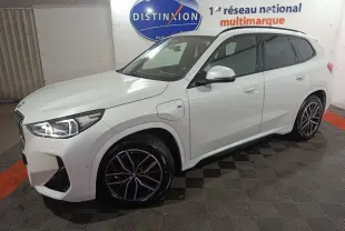 BMW X1 xDrive25e blanc en 3/4 avant droit, avec jantes noires et éclairage LED allumé.