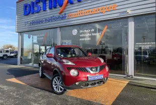 Nissan Juke rouge en 3/4 avant droit, garé devant un showroom Distinxion avec plaque personnalisée visible.