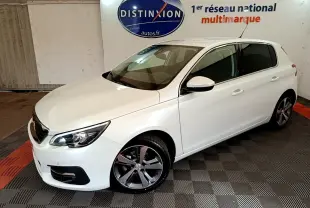Peugeot 308 blanc vue 3/4 avant droit en intérieur, avec jantes alliage et phares ellipsoïdaux visibles.